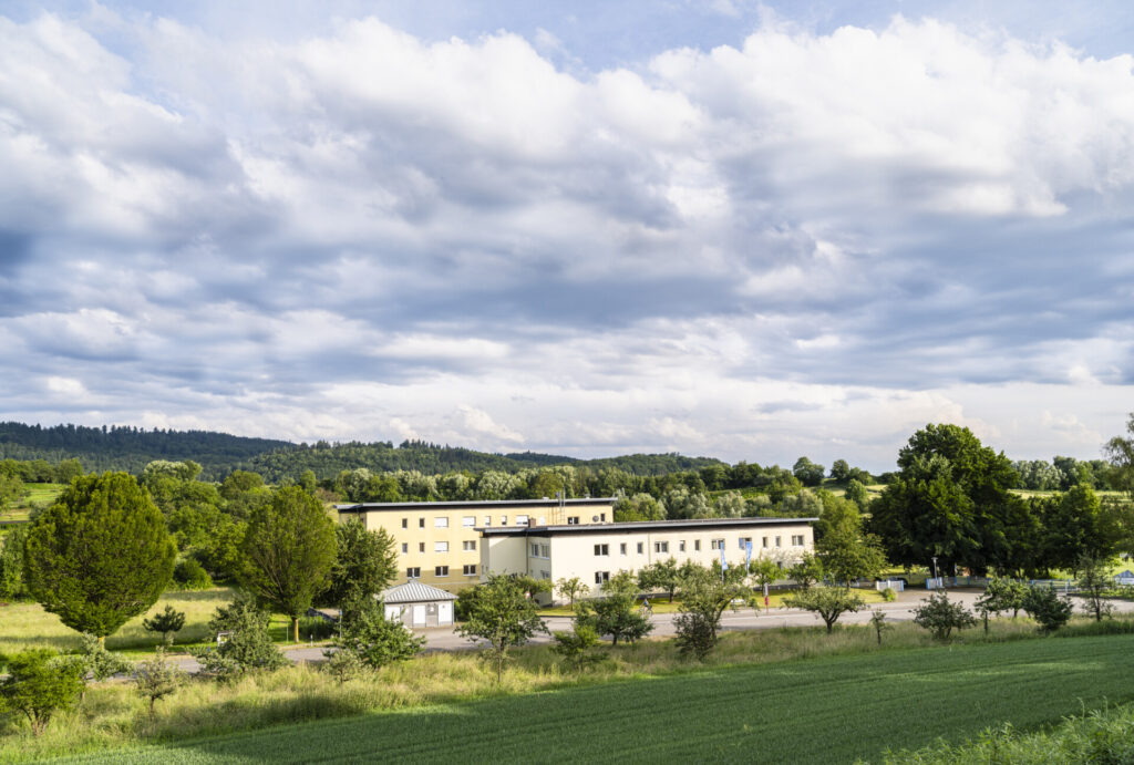 Blick von weitem über grüne Landschaft auf die Klinik